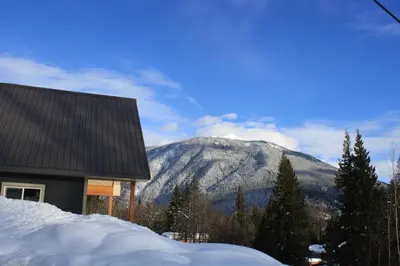 a house in the snow with a mountain in the background at Stoke Cabin by Revelstoke Vacations in Revelstoke