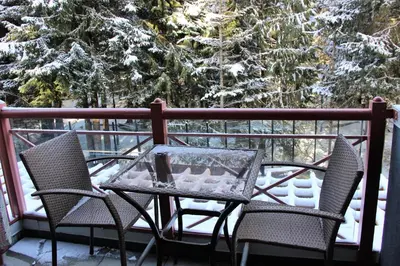 a table and chairs on a balcony with snow covered trees at Alpenglow Lodge Studio with Pool Views by MVA in Whistler