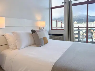 a bedroom with a white bed with a large window at Alpenglow Lodge Rainbow Look Out Studio by MVA in Whistler
