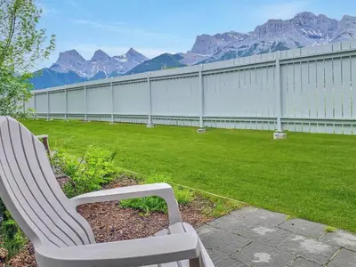 a white chair sitting in a yard with mountains at The Norquay, Pet-Friendly 2 Bed with Mtn View in Canmore