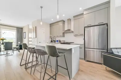 a kitchen with white cabinets and a kitchen island with bar stools at Brand New 3-Bedroom Home in a Quiet Neighborhood in Calgary