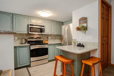 a kitchen with blue cabinets and a counter with stools at 3BR in Sunpath, King Bed, Village Location, Private Patios, Hot Tub and Pool in Whistler