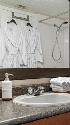 a bathroom sink with a white robe hanging in a mirror at Cozy Mountain I Hot Tub & Pool I Close 2 Lake I TV in Invermere