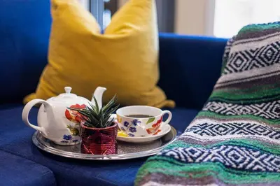 a cup of tea on a plate on a blue couch at Adorable private suite with indoor fire place in Cochrane