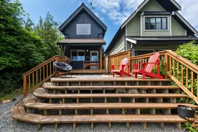 a deck with red chairs and a house at Bear Coast, Cabin with Hot Tub, Patio, and Waterview in Ucluelet