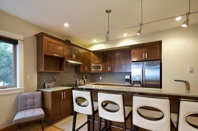 a kitchen with wooden cabinets and white bar stools at Mariner's Loft - Salt Spring Island in Ganges