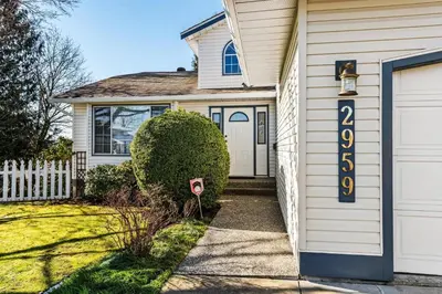 a white house with a sign on the door at B&B In Fraser Valley in Abbotsford