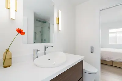a white bathroom with a sink and a vase with a flower at Steveston Village Bed and Breakfast in Richmond