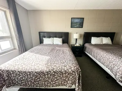 a hotel room with two beds and two windows at Beaverlodge Motor Inn in Beaverlodge