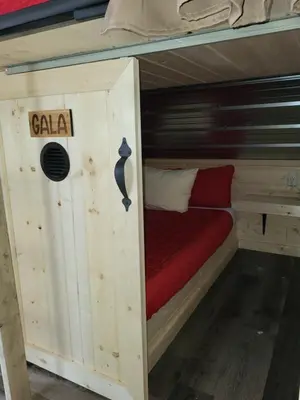 a small bed in a wooden cabin with a red mattress at THE ORCHARD (HOSTEL WITH PRIVATE BUNKS) in Radium Hot Springs