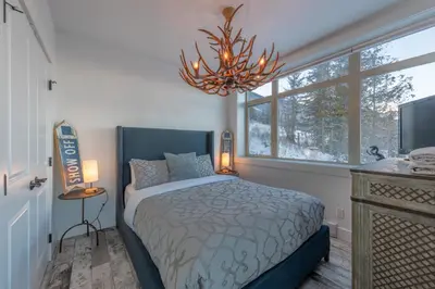 a bedroom with a bed and a window and a chandelier at Fully Renovated Ski-in/out Loft with Private Hot Tub! in Golden