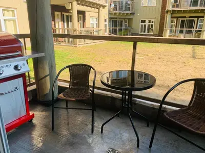 a glass table and chairs on a porch with a grill at Romantic 1-Bedroom Serviced Apartment Kitchen & AC 143 in Canmore