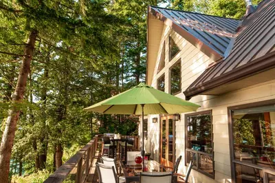 a green umbrella sitting on the side of a house at The Overlook, Luxury Lakeside Home with Dock in Harrison Hot Springs