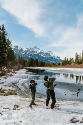 two people standing in the snow next to a river at Mount Rundle Hideaway - Pool Hot Tub in Canmore