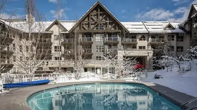 a large apartment building with a swimming pool in the snow at The best ski in ski out two bedroom condo at Aspens in Whistler