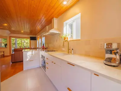 a kitchen with white cabinets and a wooden ceiling at The Perch Modern 2 Bed Cabin with Patio and Hot Tub in Ucluelet