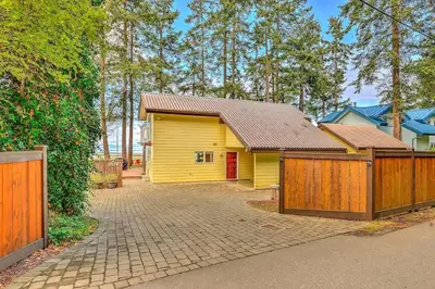 a yellow house with a fence and a driveway at Kye Bay Winter Beach House by EMR Vacation Rentals in Comox