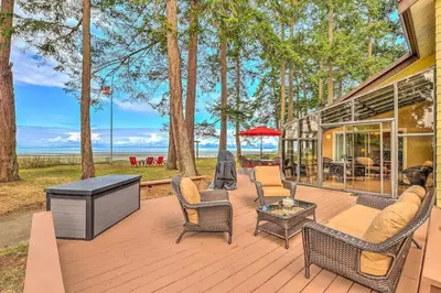 a wooden deck with chairs and a table and trees at Kye Bay Winter Beach House by EMR Vacation Rentals in Comox