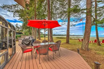 a table and chairs with a red umbrella on a deck at Kye Bay Winter Beach House by EMR Vacation Rentals in Comox