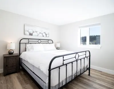 a white bedroom with a black bed and a window at NN - Flats on 4th #1 - Downtown 2-bed 2-bath in Whitehorse