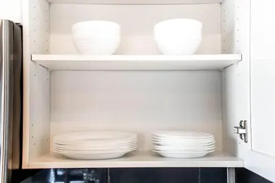 a cabinet filled with white plates and bowls at Bright Luxe Condo, AC, Top Floor, King Bed, Balcony! in Edmonton