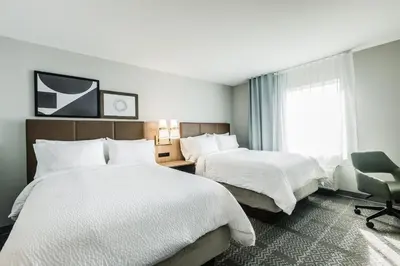 a hotel room with two beds and a chair at Staybridge Suites - Dawson Creek by IHG in Dawson Creek