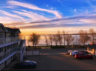 two cars parked in a parking lot with a view of the water at Raccoon Lodge Motel in Sylvan Lake
