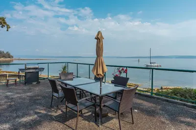 a table with chairs and an umbrella and the ocean at Sunrise Cove Apt at Inn of The Sea in Ladysmith