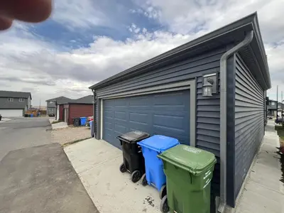 a garage with three trash cans next to a building at Cozy New Suite in NW Calgary in Calgary