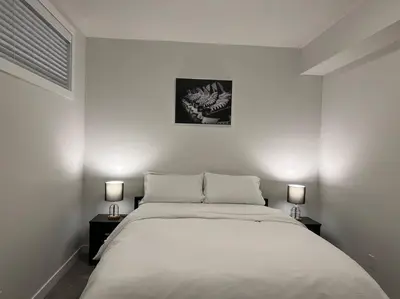 a white bedroom with a bed and two lamps at Cozy New Suite in NW Calgary in Calgary