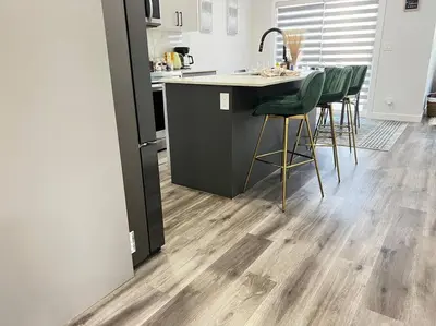 a kitchen with wooden floors and a kitchen island with green chairs at Gorgeous 6BR New Home for Families in Nisku